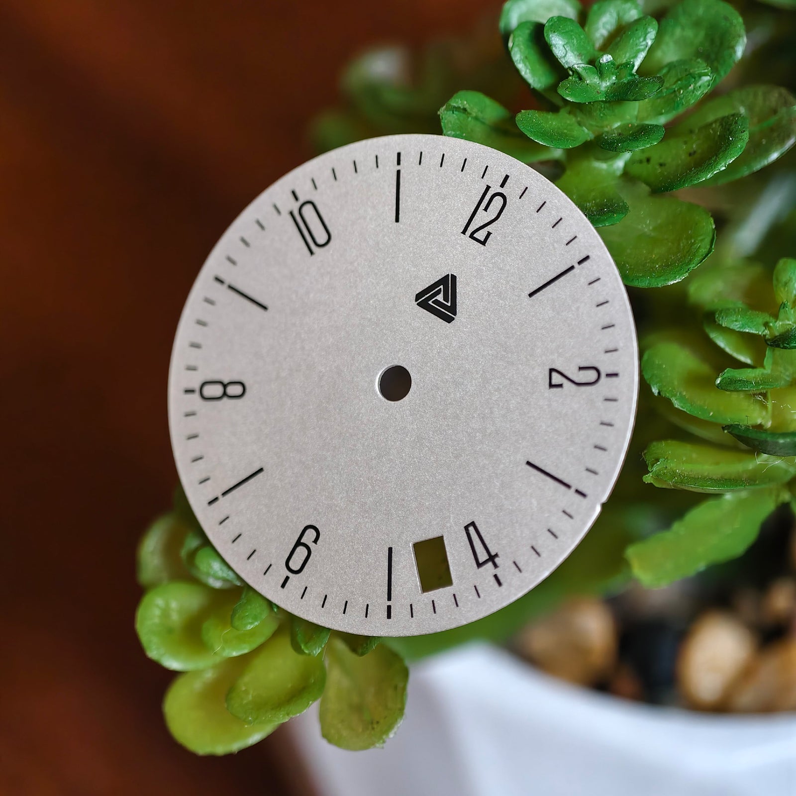 Bauhaus date dial angled view with succulent backdrop, showing date cutout and Lucius Atelier logo — Lucius Atelier