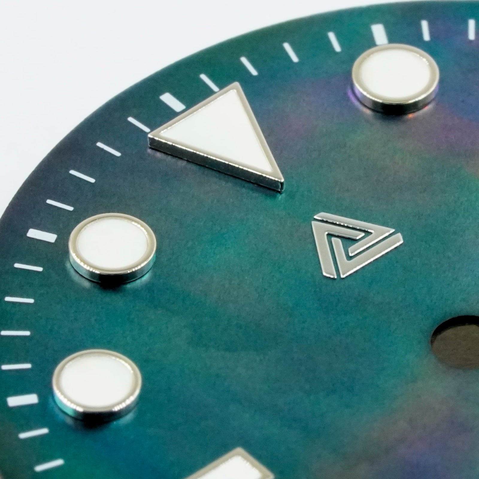 Macro of the black mother of pearl Submariner II dial — raised bevelled silver indices with cream lume fill, applied polished-silver Lucius Atelier logo, nacre reading teal and violet